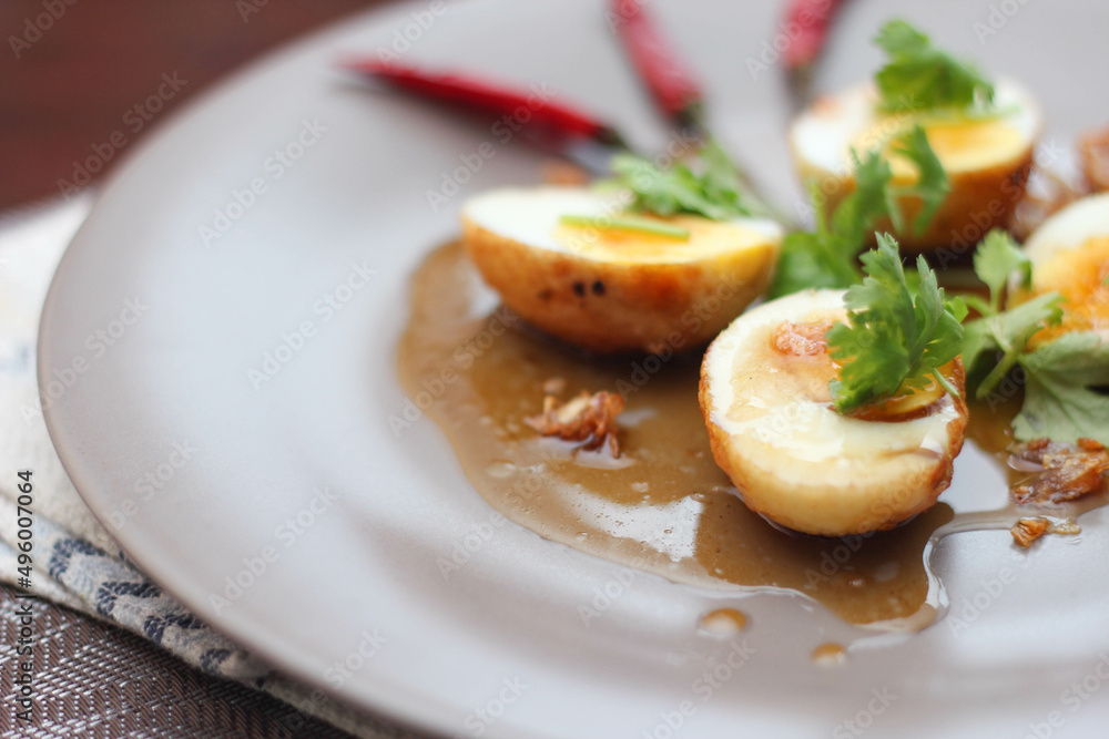 Egg with Tamarind Sauce in a white plate served on a wooden table with coriander sprinkles, is a popular local dish that Thai people eat. Egg with Tamarind Sauce in a white plate served on a wooden table with coriander sprinkles, is a popular local dish that Thai people eat.
