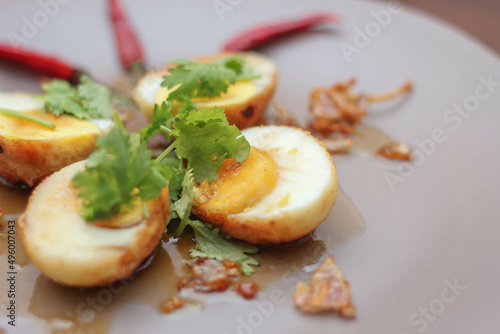 Egg with Tamarind Sauce in a white plate served on a wooden table with coriander sprinkles, is a popular local dish that Thai people eat.