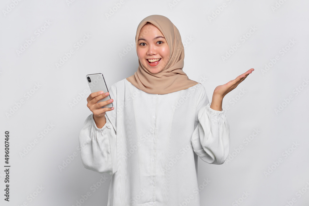 Excited young Asian Muslim woman using a mobile phone and celebrating success, getting good news isolated over white background Excited young Asian Muslim woman using a mobile phone and celebrating success, getting good news isolated over white background