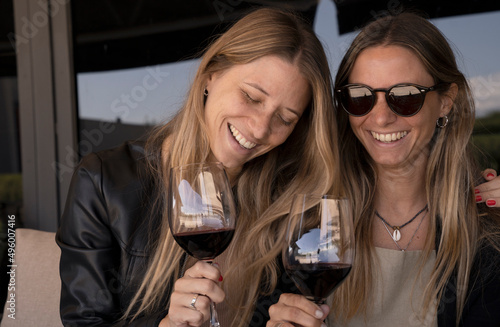 Two young woman having fun, laughing and smiling while holding a cup of red wine. 