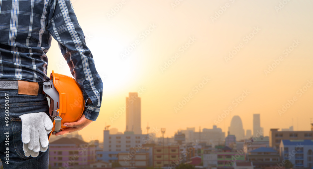 Back view of the business or engineering smart holding orange helmet on a city background. Back view of the business or engineering smart holding orange helmet on a city background.