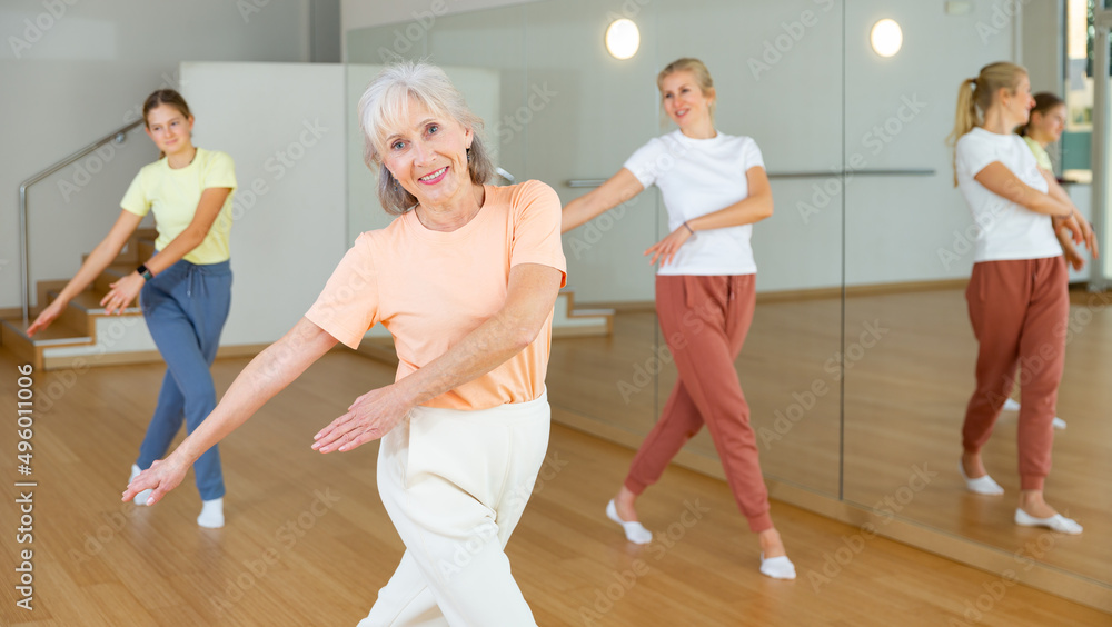 Elderly woman learning aerobic dance with her younger relatives in studio.