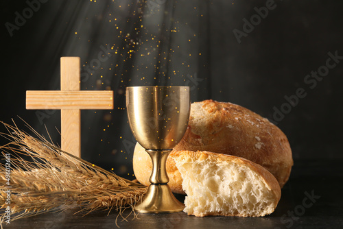 Chalice of wine with bread and cross on dark background. Holy Communion concept photo