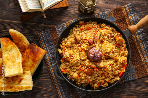 Frying pan of tasty Asian pilaf and flatbread on wooden background