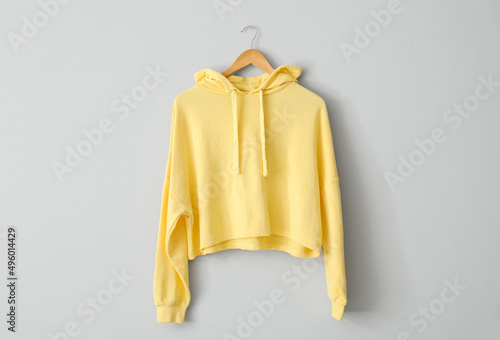 Stylish yellow hoodie hanging on light wall photo