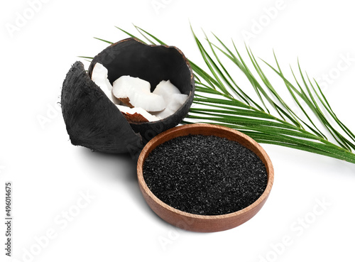 Bowl with coconut activated carbon and shells on white background photo