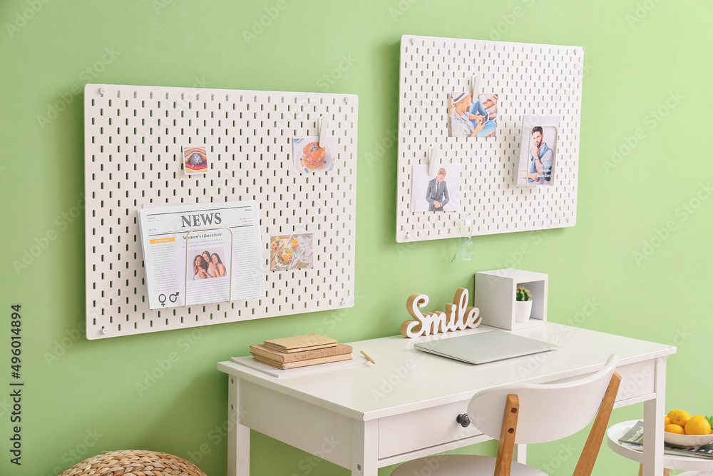 Modern workplace with different supplies and peg board on green wall Modern workplace with different supplies and peg board on green wall