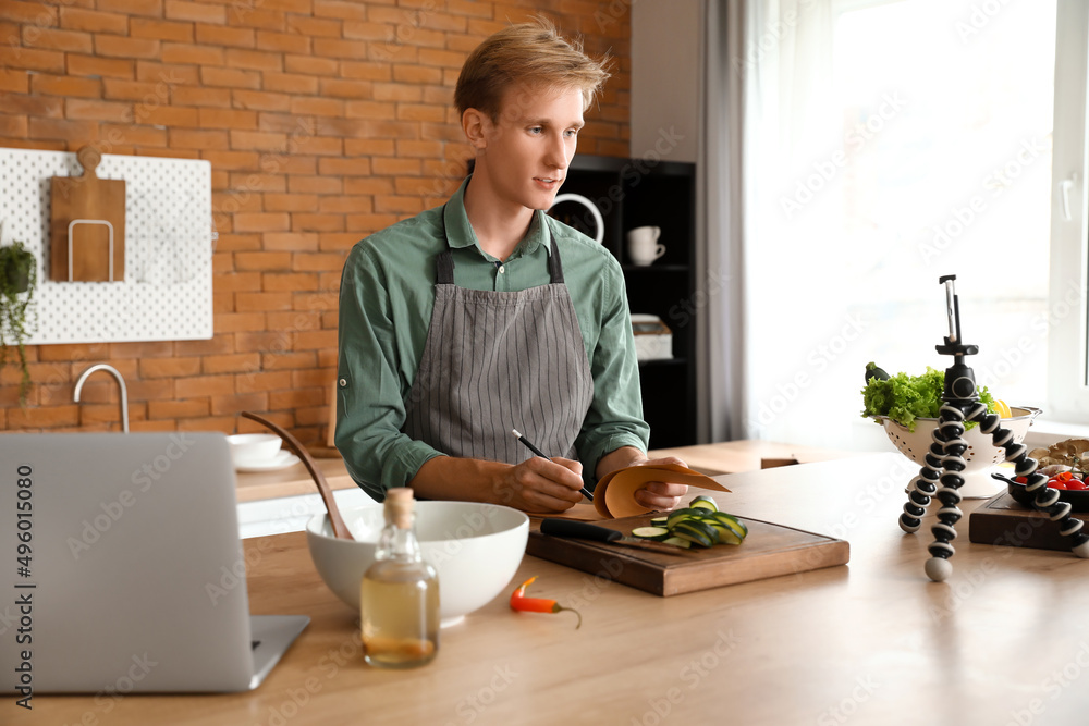 Young man making notes from cooking video tutorial in kitchen Young man making notes from cooking video tutorial in kitchen