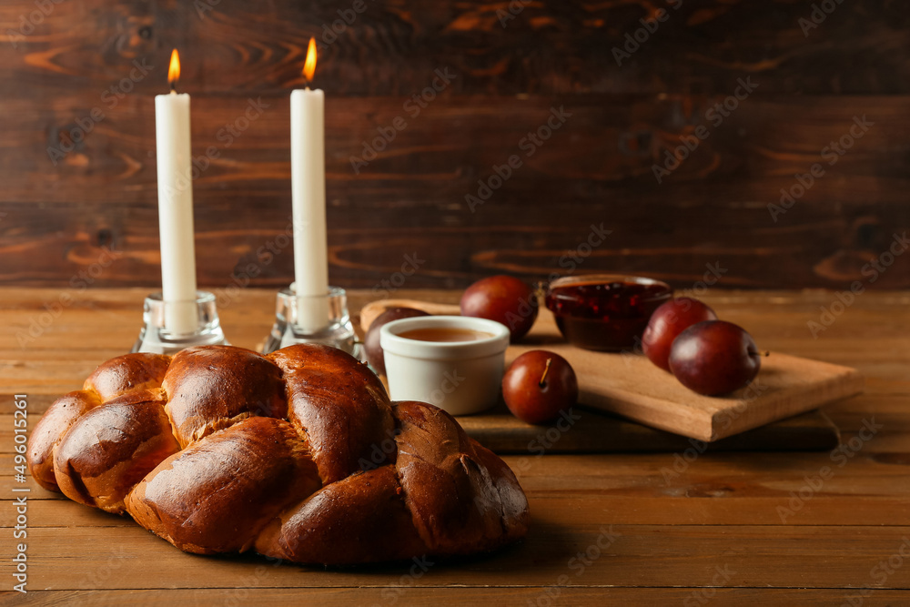 Traditional challah bread with glowing candles on wooden background