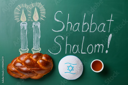 Drawn glowing candles and written text SHABBAT SHALOM with traditional challah bread and Jewish cap on chalkboard