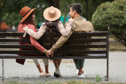Fototapete Man and two beautiful women sitting on bench in park