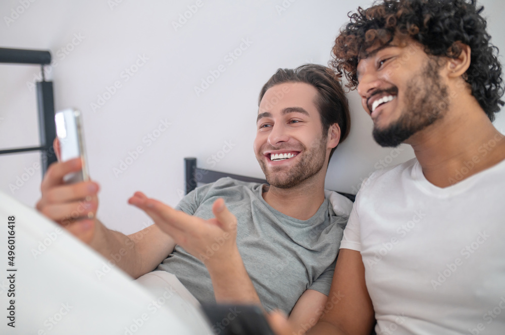 Fototapeta premium Joyful guy demonstrating photos on the cellphone to his companion