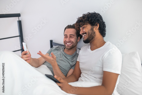 Cheerful man pointing at his cellphone screen to his boyfriend
