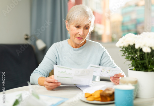 Portrait of modern stylish senior woman sitting at home table, reading papers with interest.