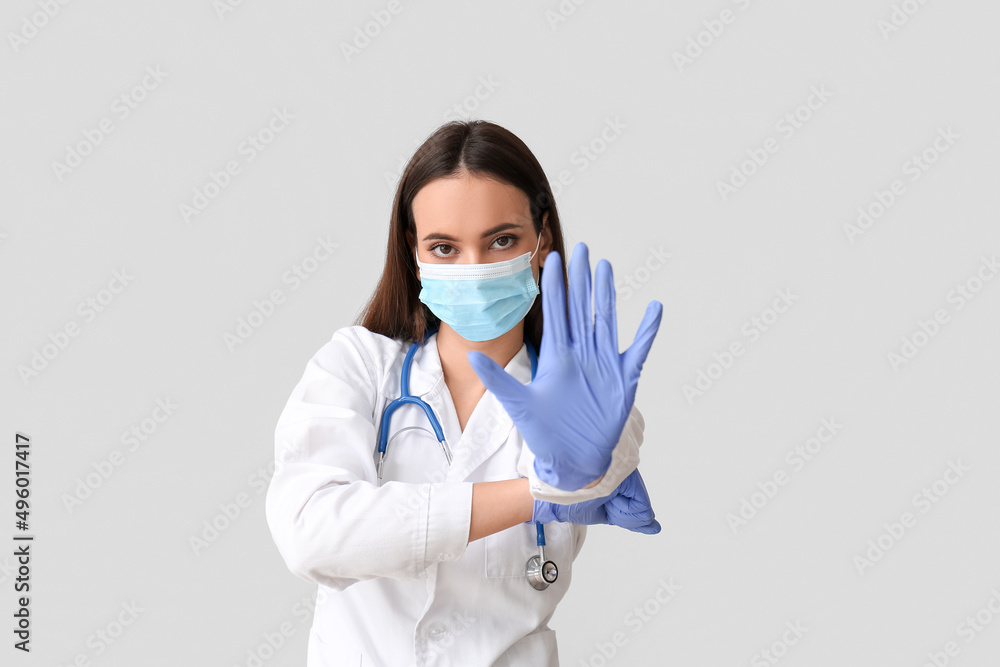 Young female doctor in medical mask showing stop gesture on light background. Immunity concept Young female doctor in medical mask showing stop gesture on light background. Immunity concept