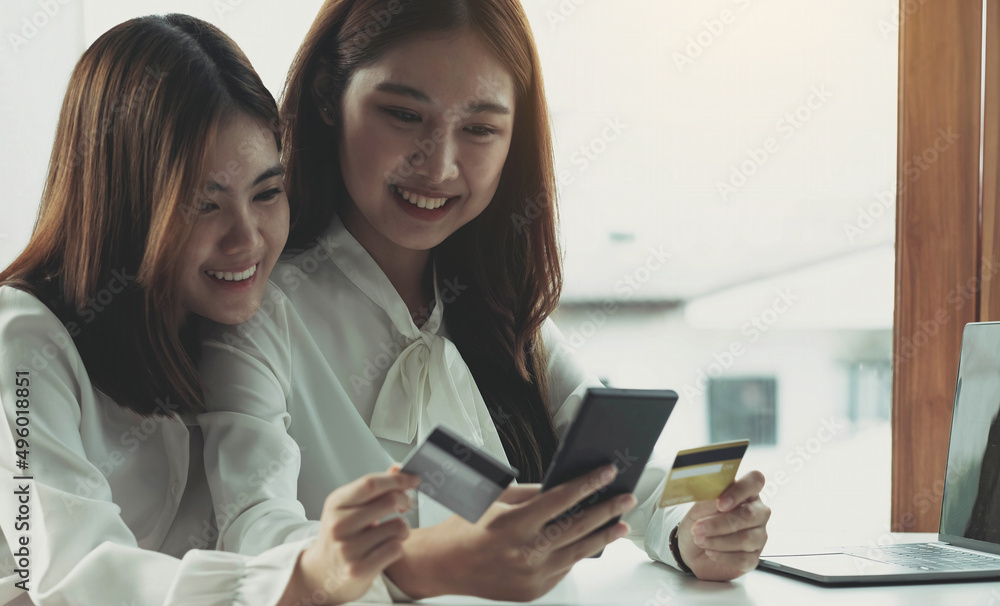 Two young Asian women hold credit cards and happily use their mobile phones for online shopping. business concept and technology digital marketing casual lifestyle Two young Asian women hold credit cards and happily use their mobile phones for online shopping. business concept and technology digital marketing casual lifestyle