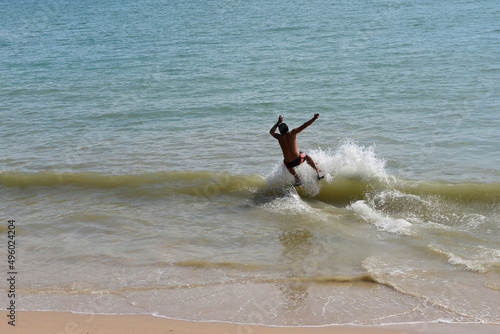 Man on a skimboard catching a wave in a beach in Aonang, Krabi, Thailand