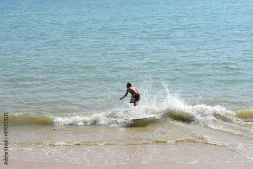 Man on a skimboard catching a wave in a beach in Aonang, Krabi, Thailand