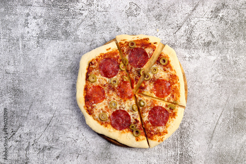 Sliced homemade pizza with pepperoni and olives on a dark grey background. Top view, flat lay