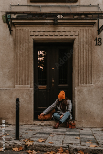 Young woman is sitting near beautiful old building with cat in fall season