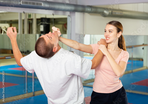 Young woman practicing basic self-defense techniques while training in gym with male partner, performing palm heel strike in chin..