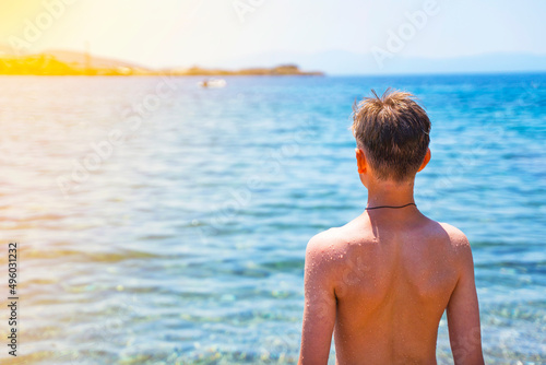  handsome teenage boy on the beach in a swimsuit looks at the sea. Attractive young man on the background of the sea.