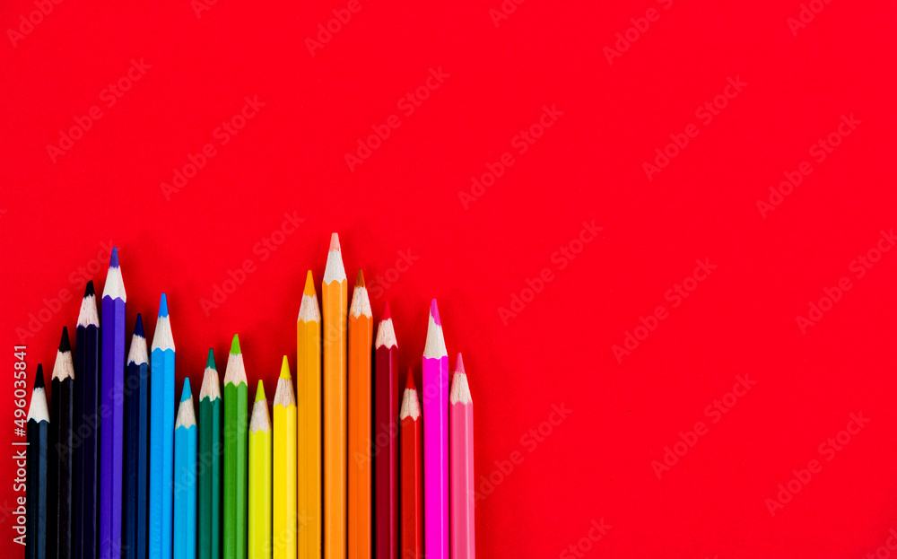 A row of color pencils on red background A row of color pencils on red background
