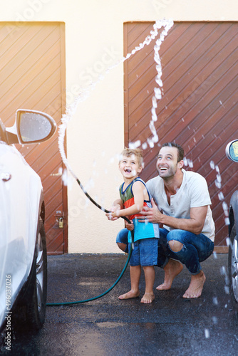 Theyre having so much fun. Full length shot of a father and son playing with a hosepipe while washing a car together.