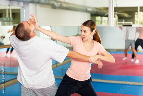 Young woman practicing basic self-defense techniques while training in gym with male partner  performing palm heel strike in chin..