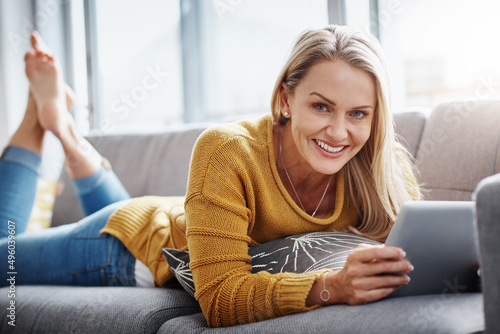 My go to gadget for downtime entertainment. Portrait of an attractive mature woman using a digital tablet while relaxing on the sofa at home.