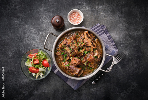 Beef oxtails stew with wine and vegetables. Dark background. Top view.