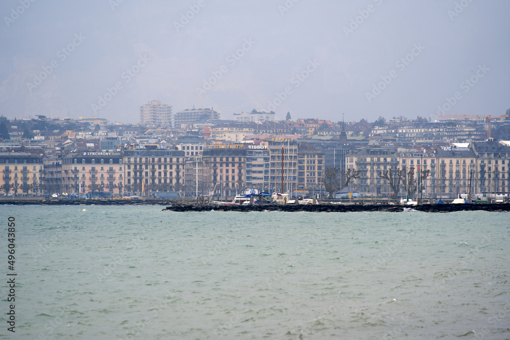 Border of Lake Geneva at City of Geneva with cityscape in the background on a gray and cloudy spring day. Photo taken March 18th, 2022, Geneva, Switzerland.