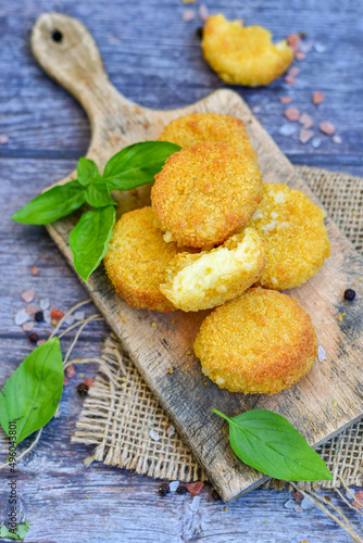 Vegetarian Cheese oven baked Croquette with fresh basil on Wooden background. Yellow cheese nuggets