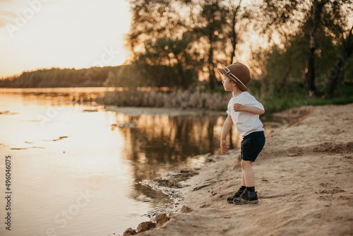 A little boy in a hat throws hay and laughs in the summer on a sunny day