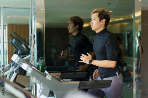 Active Asian sportsman making a cardio exercise by running on the treadmill machine in a fitness or gym.