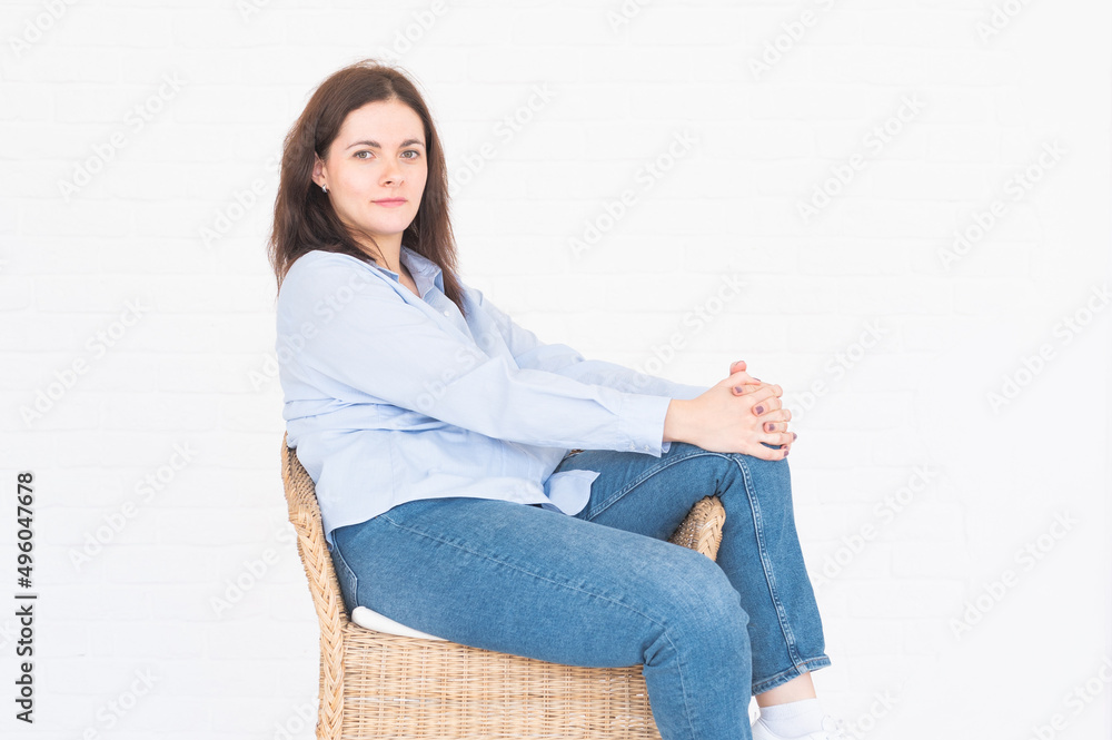 Stylish brunette plus-size model woman posing sitting on chair in studio on white background Stylish brunette plus-size model woman posing sitting on chair in studio on white background