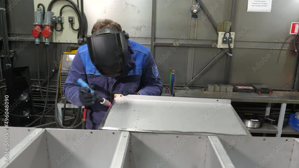 A welder in protective clothing and a mask works with a welding machine A welder in protective clothing and a mask works with a welding machine