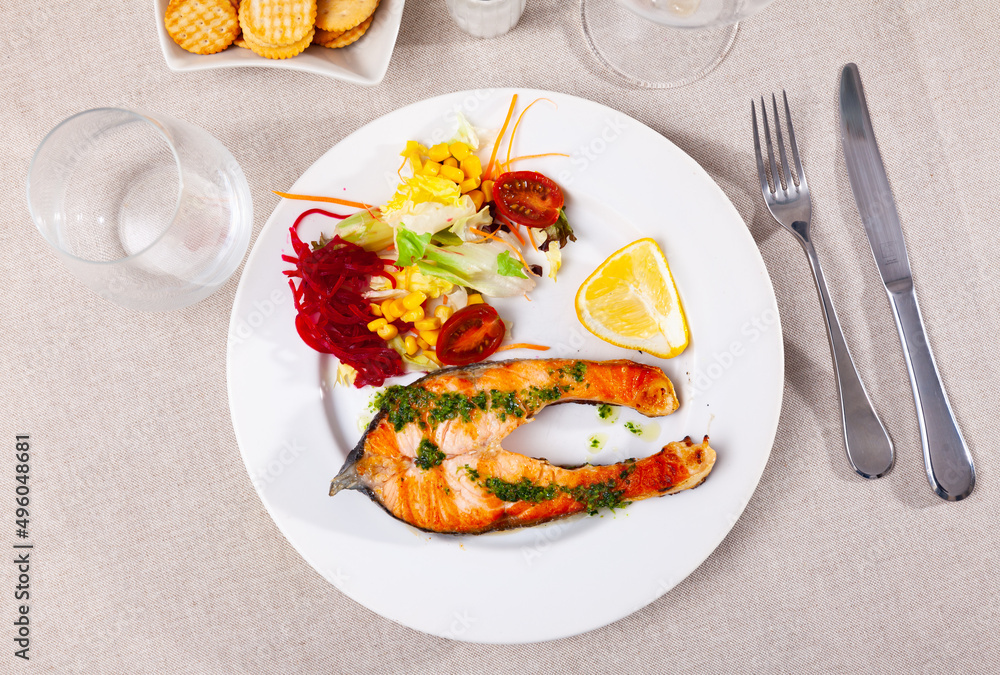 Appetizing roasted salmon steak with a light vegetable salad made from corn, lettuce leaves and grated beetroot, served ..with a slice of lemon and drizzled sauce