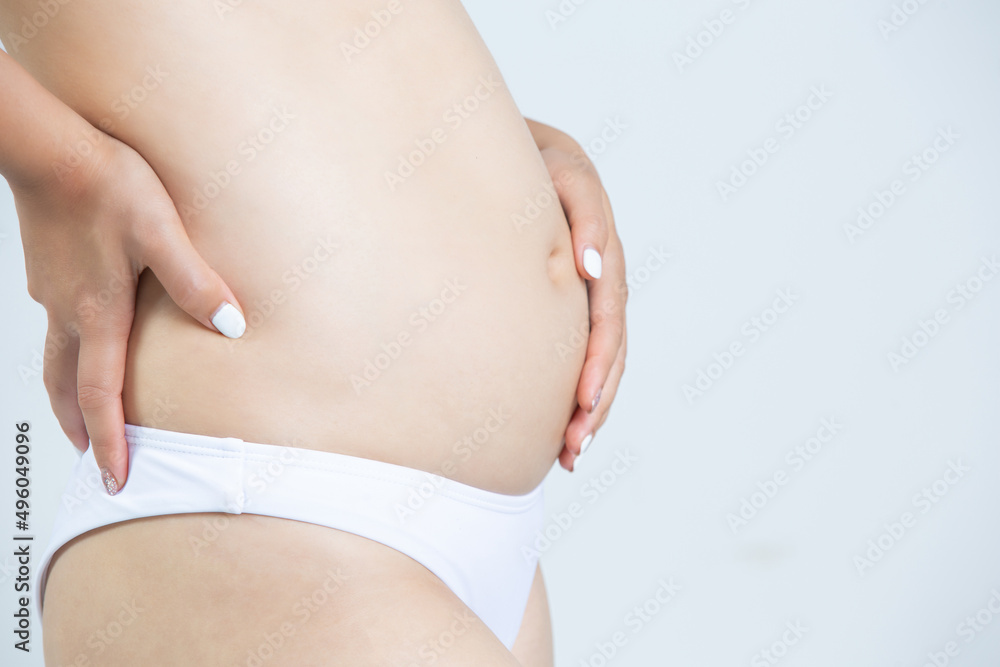 woman caressing her belly while standing against a white background