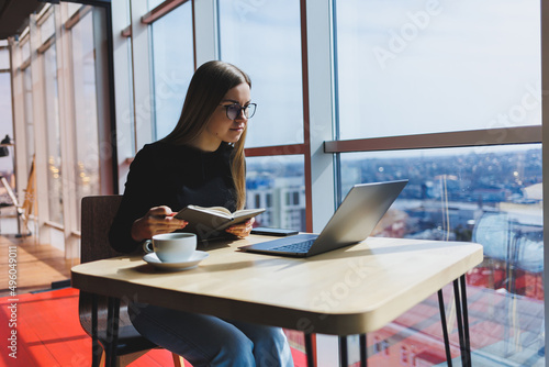 Online work in a cafe. Happy girl in casual clothes and glasses using a laptop. Remote work or education with modern digital technologies for a comfortable lifestyle in the city.