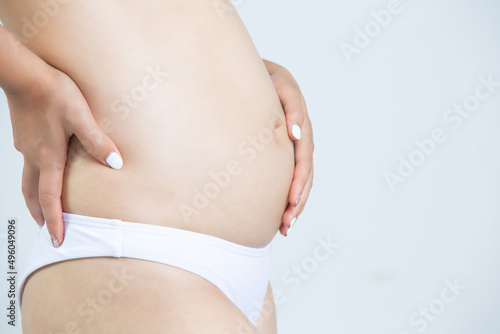 woman caressing her belly while standing against a white background