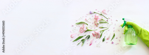 Spring cleaning concept with hand wearing glove and holding a sprayer over floral white wooden background