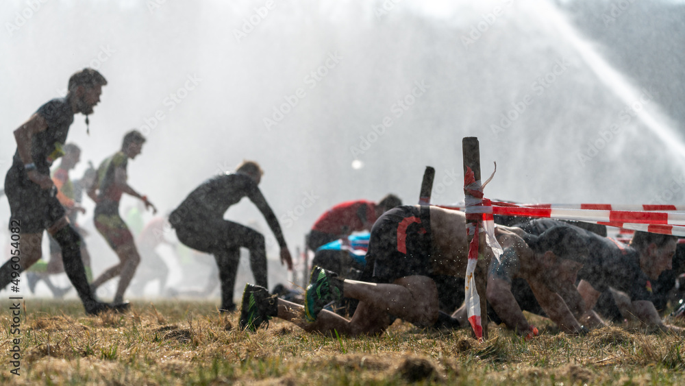 Fototapeta premium Athletes run under a crawling obstacle in water spray during obstacle course race 