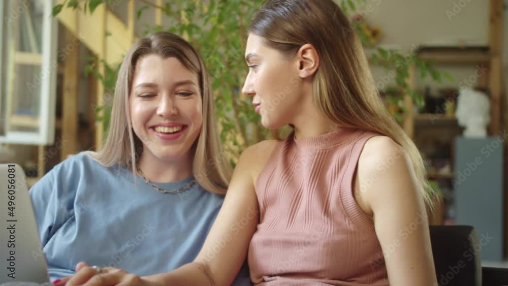 Two young beautiful ladies are searching through the Internet on the laptop, discussing and smiling Two young beautiful ladies are searching through the Internet on the laptop, discussing and smiling