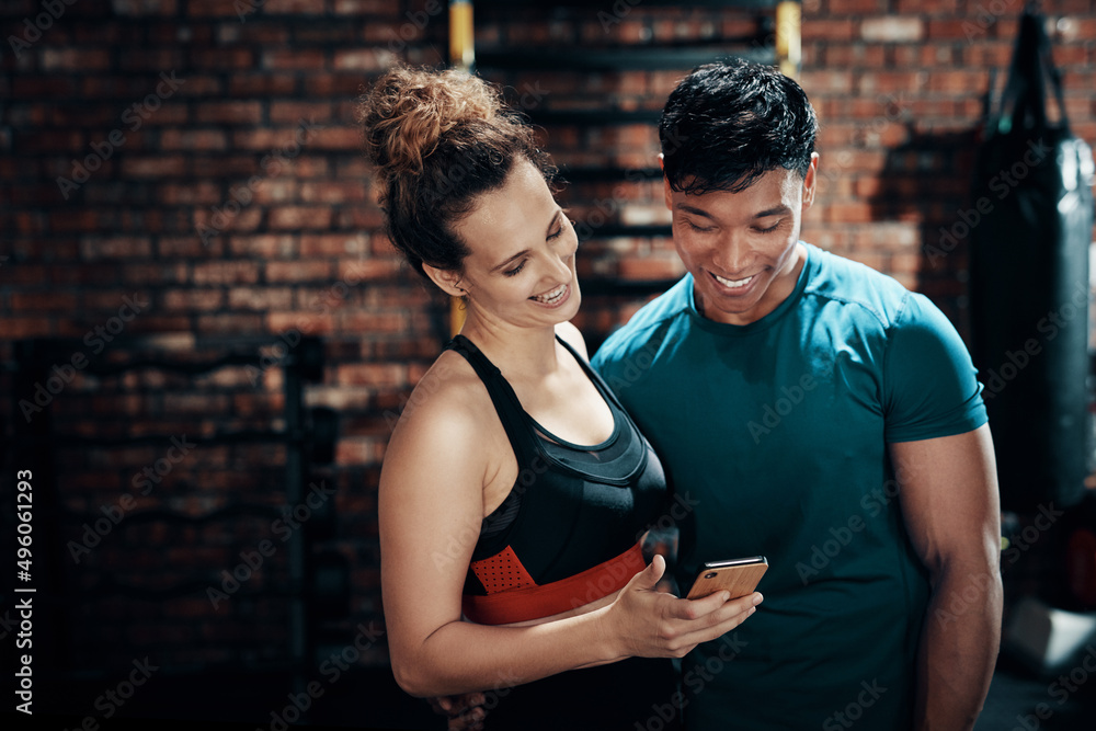 Naklejka premium Dont we just look cute here. Cropped shot of two young sportspeople using a smartphone together in a gym.