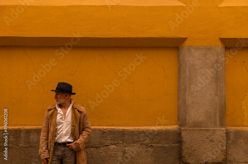 Portrait of adult man in hat and coat against yellow wall on street. Madrid, Spain