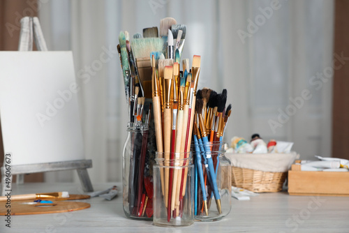 Glass jars with many different paintbrushes on white wooden table indoors
