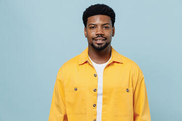 Young smiling handsome attractive happy man of African American ethnicity 20s wearing yellow shirt look camera isolated on plain pastel light blue background studio portrait. People lifestyle concept.