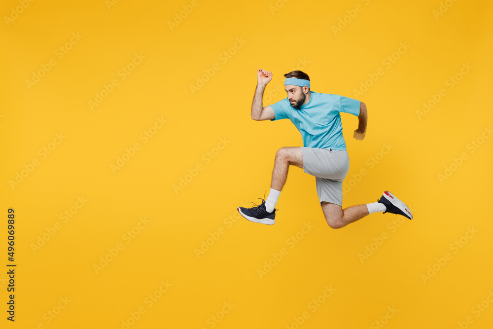 Full body side view strong young fitness trainer instructor sporty man sportsman wear headband blue t-shirt jump high run fast isolated on plain yellow background. Workout sport motivation concept