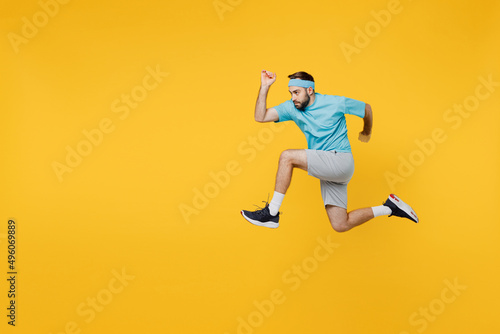 Fotografia Full body side view strong young fitness trainer instructor sporty man sportsman wear headband blue t-shirt jump high run fast isolated on plain yellow background